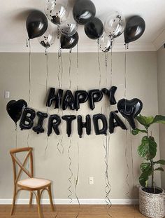 black and white balloons that say happy birthday hanging from the ceiling above a wooden chair