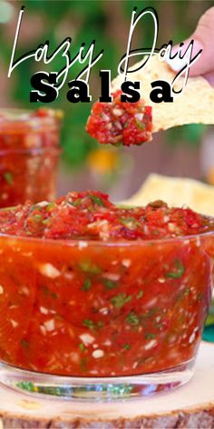 a person dipping salsa into a bowl with a tortilla chip in the background