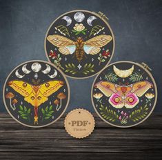 three embroidery kits with moths and flowers on them, one in the shape of a circle