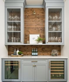 a kitchen cabinet with wine glasses and bottles on it's doors, in front of a wood paneled wall