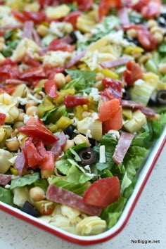 a salad with corn, tomatoes, olives and other toppings in a red dish