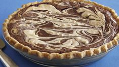 there is a pie with chocolate swirls in the pie pan next to a knife and fork