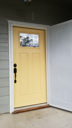 a yellow door is open in front of a gray house