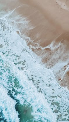 an aerial view of the ocean with waves crashing on the shore and footprints in the sand