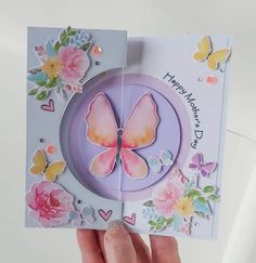 someone holding up a card with a butterfly on it and flowers around the edges that say happy birthday