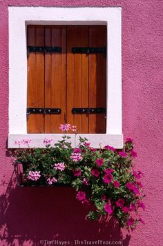 a pink building with two wooden doors and flowers in the window sill below it