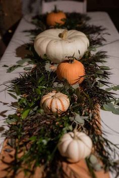 several pumpkins and greenery are arranged on a long white tablecloth with green leaves