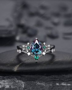 a blue and green ring sitting on top of a black stone covered in white diamonds