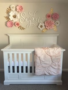 a baby crib with pink and white flowers on the wall next to it's name