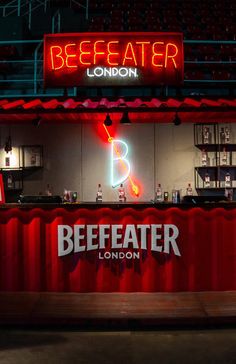 the bee eater london bar is lit up with neon signs and red curtains behind it