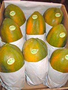 a box filled with lots of ripe mangoes in white paper cups on top of each other