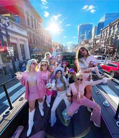 a group of women in pink outfits posing for a photo on a street with cars and buildings behind them