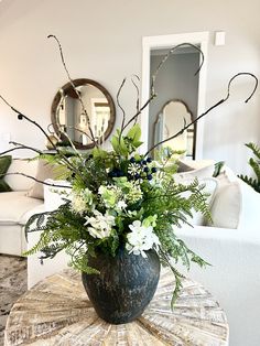 a vase filled with flowers sitting on top of a table next to a couch and mirror