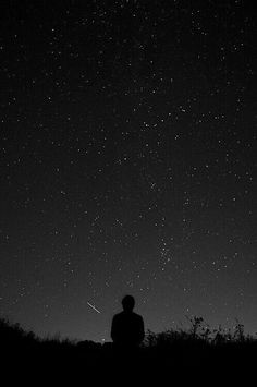 a man sitting on top of a grass covered field under a night sky filled with stars