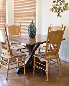 a dining room table with chairs and a vase on top of it in front of a window