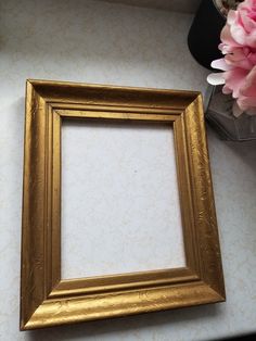 a gold frame sitting on top of a table next to a vase with pink flowers