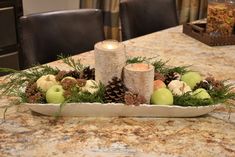 an arrangement of apples, pine cones and candles sits on a table in front of a candle holder