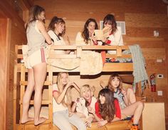 a group of young women sitting on top of bunk beds in a room with wooden walls