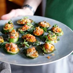 a person holding a plate full of stuffed peppers with sauce on them and garnished with herbs