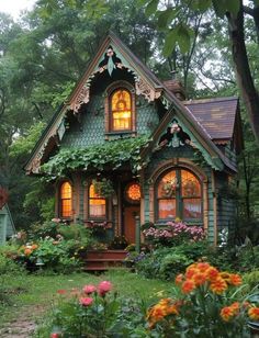 a small green house with lots of flowers in the front yard and trees around it