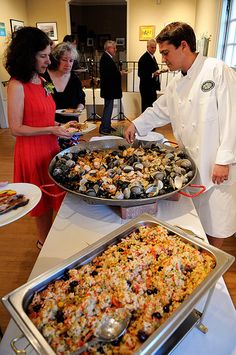 two people in white coats are serving food to some other people at a buffet table