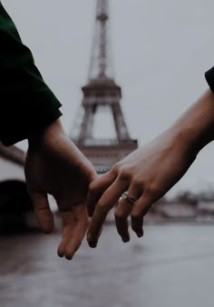 two people holding hands in front of the eiffel tower