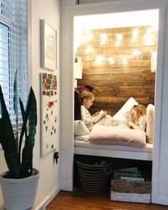 two children are sitting on a bed in their room with lights strung above the headboard