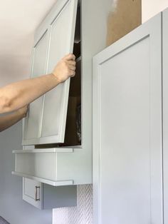 a person is holding the door open to an upper cabinet in a kitchen that's being painted white