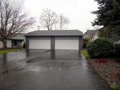 an empty driveway with two garages and trees in the background on a cloudy day