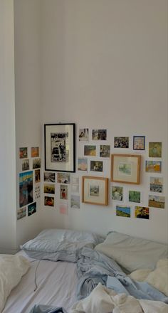 an unmade bed with many pictures on the wall