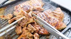 the meat is being grilled on the grill with tongs and an electric heater