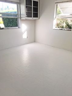 an empty room with white tile floors and two windows in the corner, all painted white