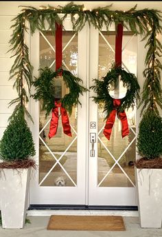 two white planters with wreaths and red bows on them are sitting in front of a door