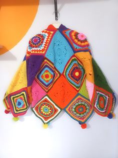 a multicolored crocheted blanket hanging from a hook on a white wall