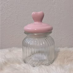 a glass jar with a pink lid sitting on top of a white fur covered floor