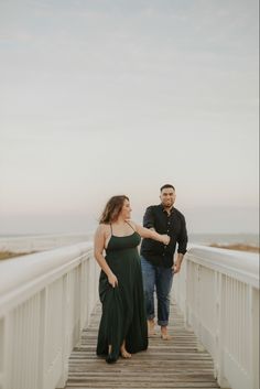 two people standing on a bridge near the ocean and one person is holding his hand