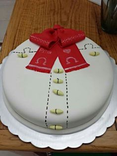 a white cake with a red ribbon on it sitting on top of a wooden table