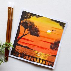 an orange sunset painting with two pencils next to it and a potted plant