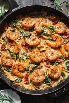 a skillet filled with shrimp and spinach on top of a wooden table,