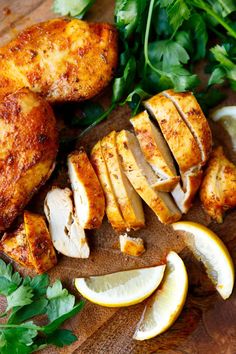 sliced chicken, lemons and parsley on a cutting board next to fresh herbs