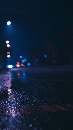 the street is wet from rain at night with many lights in the dark behind it