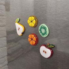 four different fruit shaped buttons sitting on top of a metal surface with white and green accents