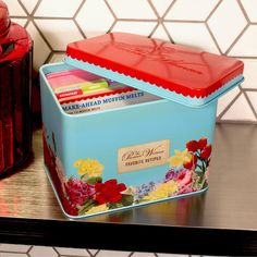 a blue tin with red lid sitting on top of a table next to a canister