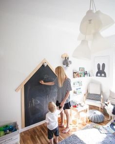 a woman and child writing on a blackboard in a room with white walls, hardwood floors and blue rugs