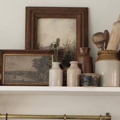 a shelf filled with vases and other items on top of a white wall next to a framed painting