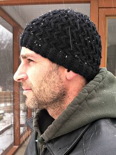 a man wearing a black knitted beanie looking out the window on a snowy day