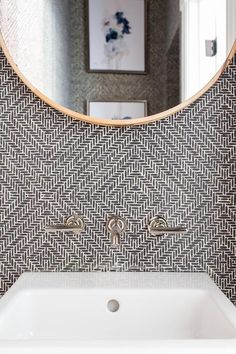 a bathroom sink under a round mirror in front of a wall mounted faucet