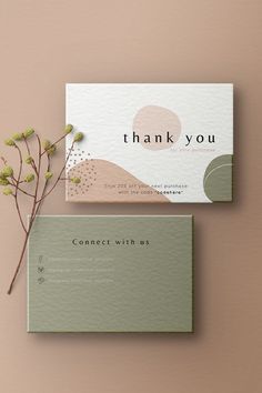 two business cards with the words thank you on them next to a plant in front of it