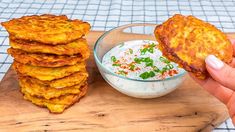 a person is holding up some food on a cutting board next to a bowl of dip