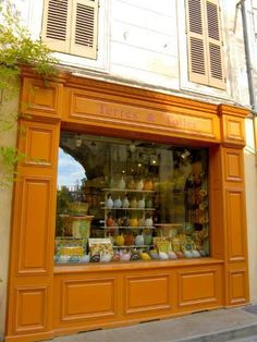 an orange store front with lots of different items in the display window and shutters open